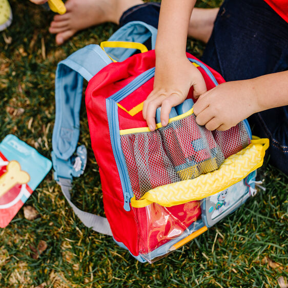 Child's hands interacting with a red and blue PAW Patrol backpack set on grass for Melissa and Doug 33271