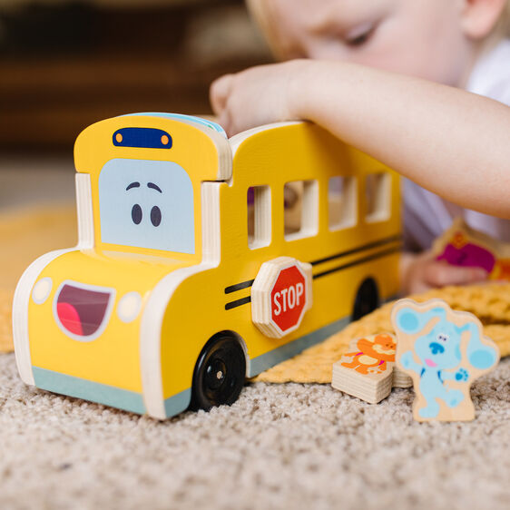 Yellow wooden school bus toy with blue accents, near a child's hands for Melissa and Doug 33011