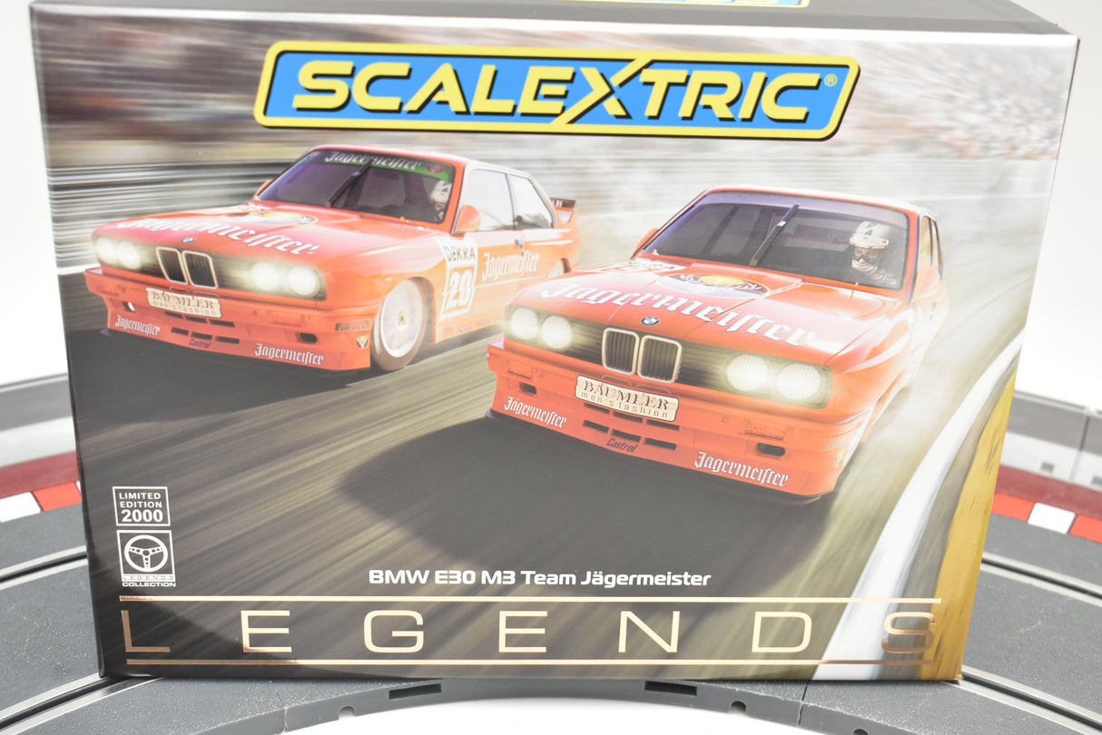 Two slot car BMW E30 M3 race cars in Jagermeister livery on a box for Scalextric C4110A