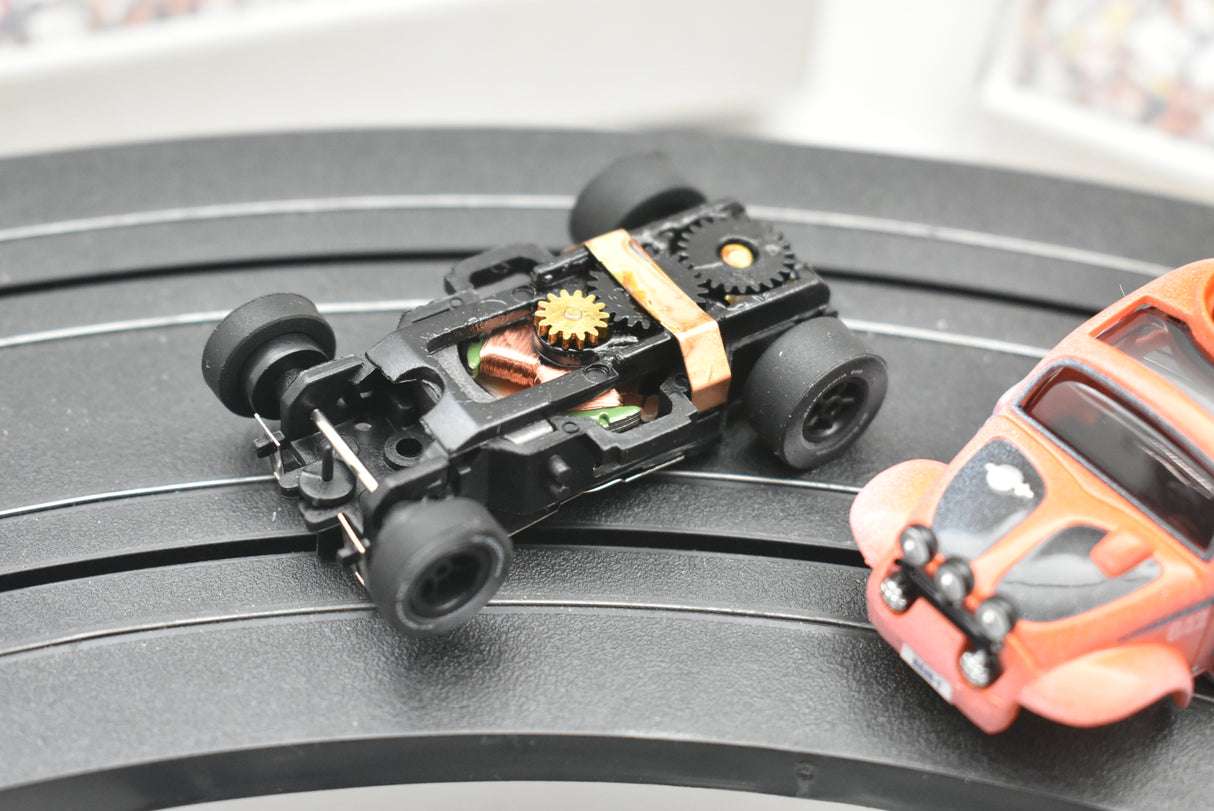 Black toy car and orange VW Beetle toy on a dark surface for Auto World SC011
