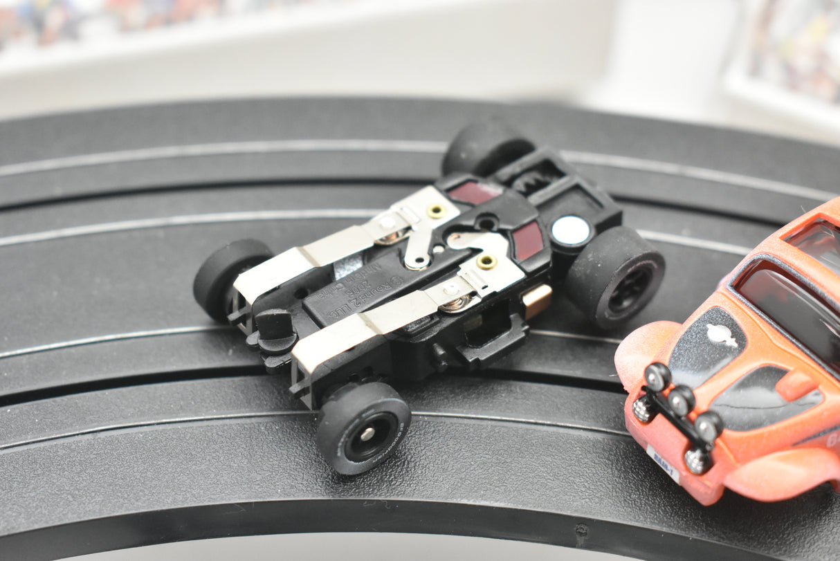 Small black and orange remote-controlled cars on a dark track for Auto World SC011