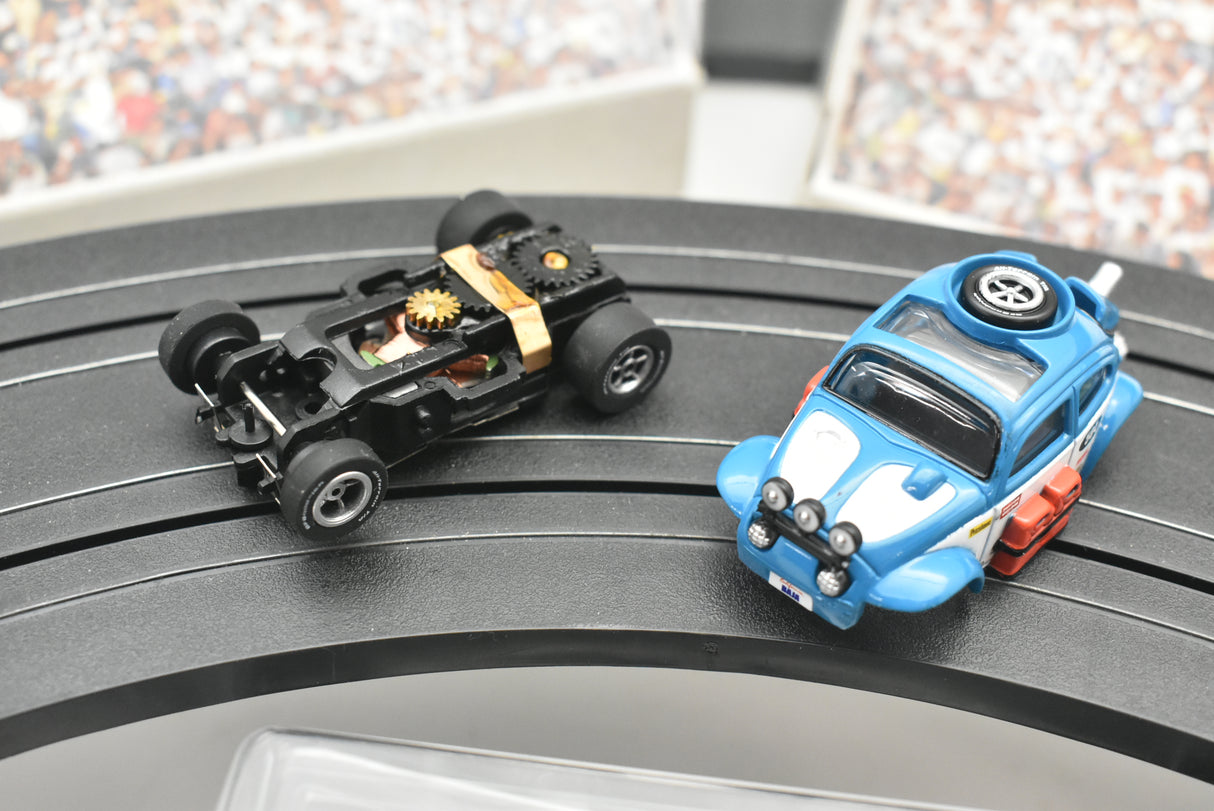 Two remote-controlled vehicles, one black off-road, one blue Beetle, on a dark surface for Auto World SC012