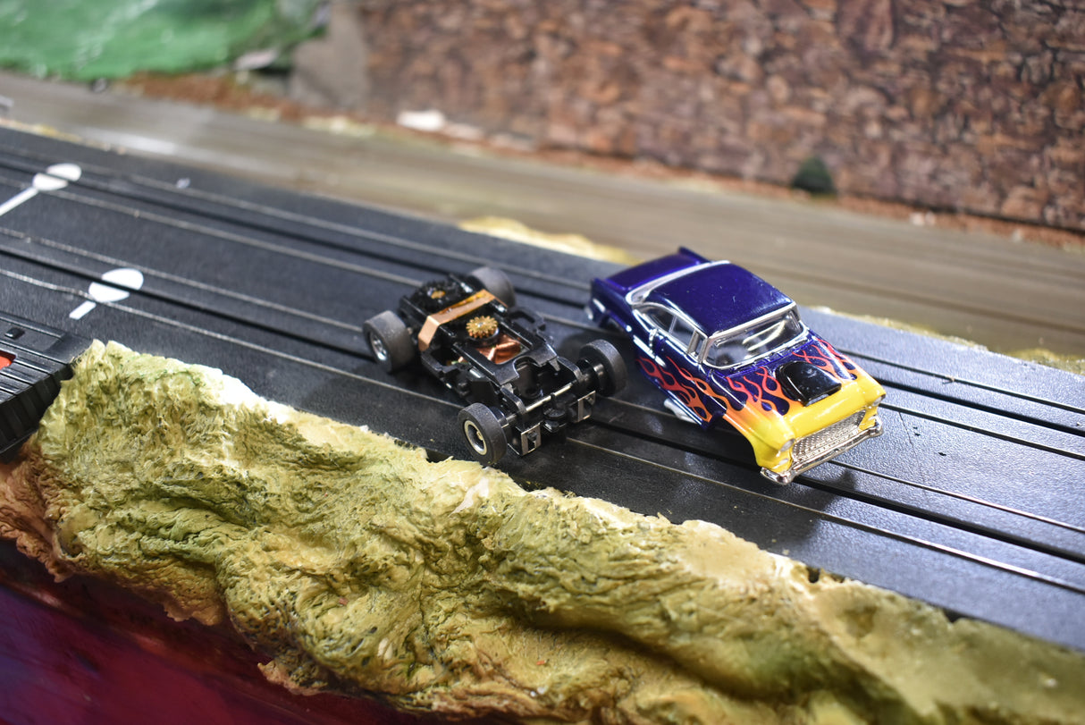 Two slot cars on a track: a black Chevy and a blue/yellow Chevy for Slot Car 1:64 CP7726