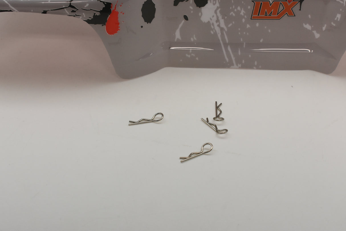 Small metal hooks laid out on a surface near a gray truck body for IMEX R/C parts IMX18590