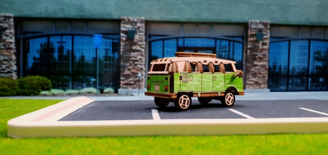 Wooden VW bus toy car on asphalt in front of modern building for Wooden City 502380