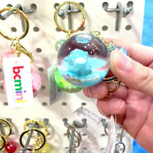 Blue and white cloud key charm held in hand against a display of other charms for BC Mini 12056