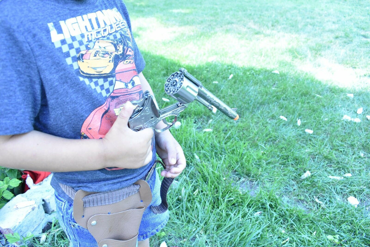 Boy holding a toy pistol and holster set outdoors on green grass for Parris Toys 4711, rear view