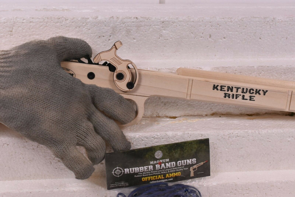 Hand holding a wooden toy rifle next to ammo packaging for Magnum Rubber Band Guns GL2KR