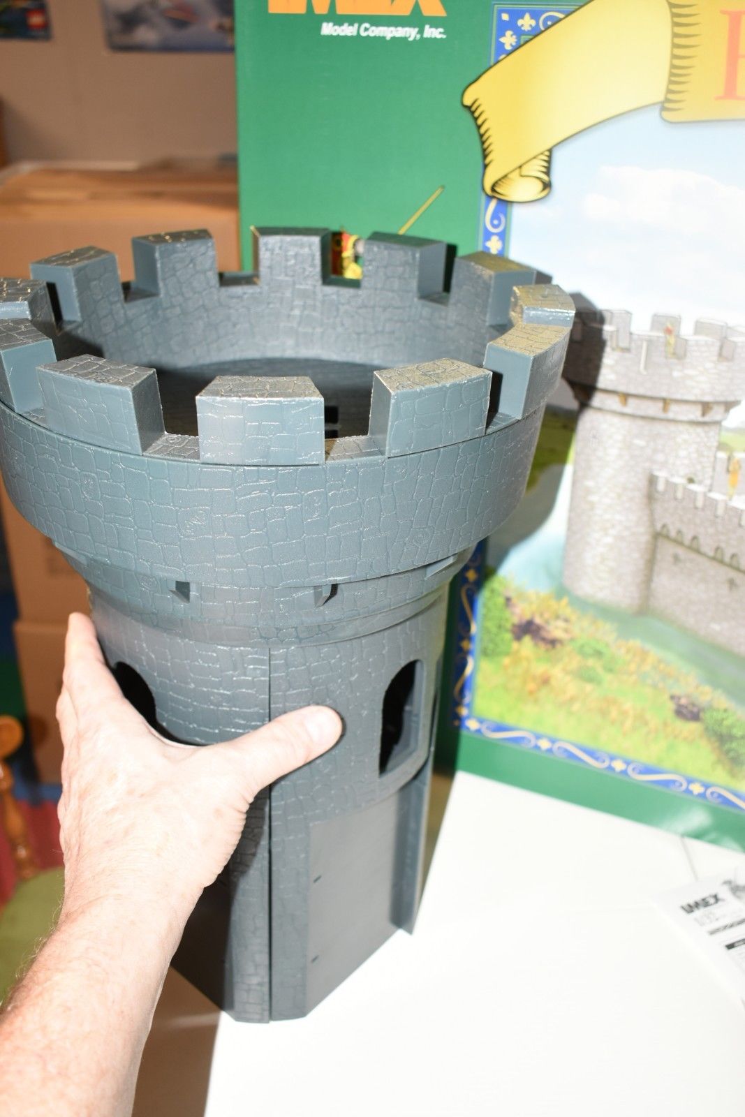 Hand holding a gray, crenelated castle turret model piece for IMEX IMX3282
