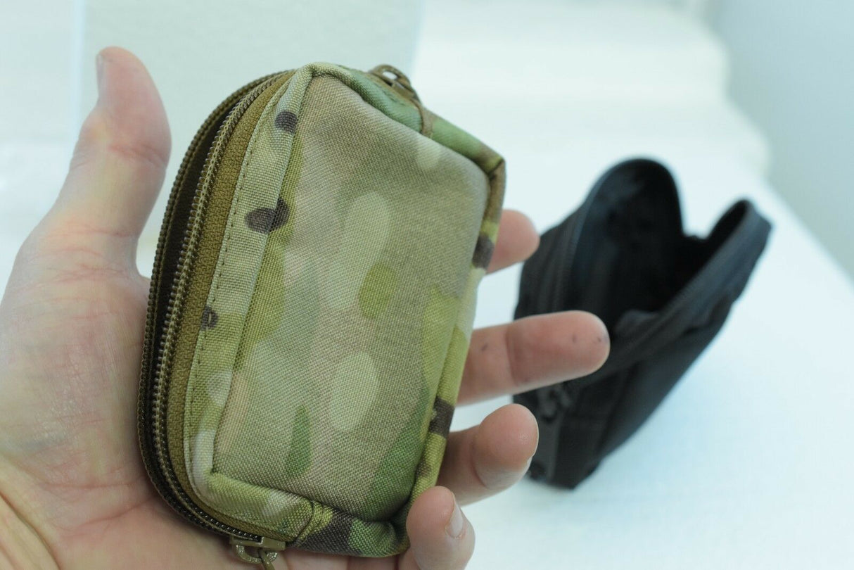 Camo-patterned zippered wallet held in a hand next to a black wallet for While The Cigars Lit WTCL001
