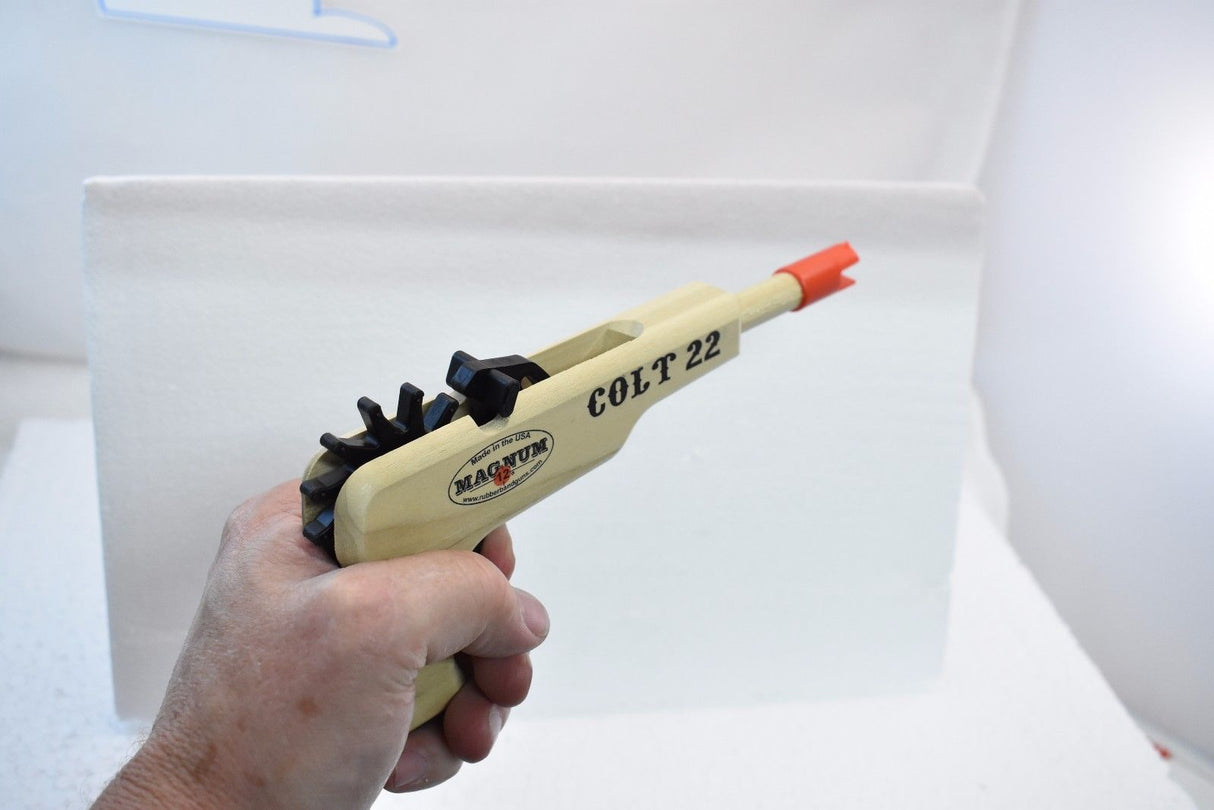 Wooden toy pistol with black bands and orange tip, held by a hand for Magnum Rubber Band Guns GL2C22
