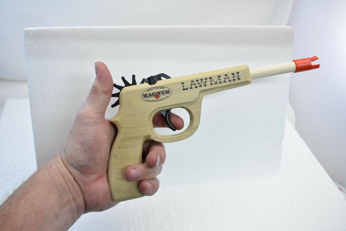 Hand holding a toy pistol with red tips and a visible "LAWMAN" marking for Magnum Rubber Band Guns GL2LWMN