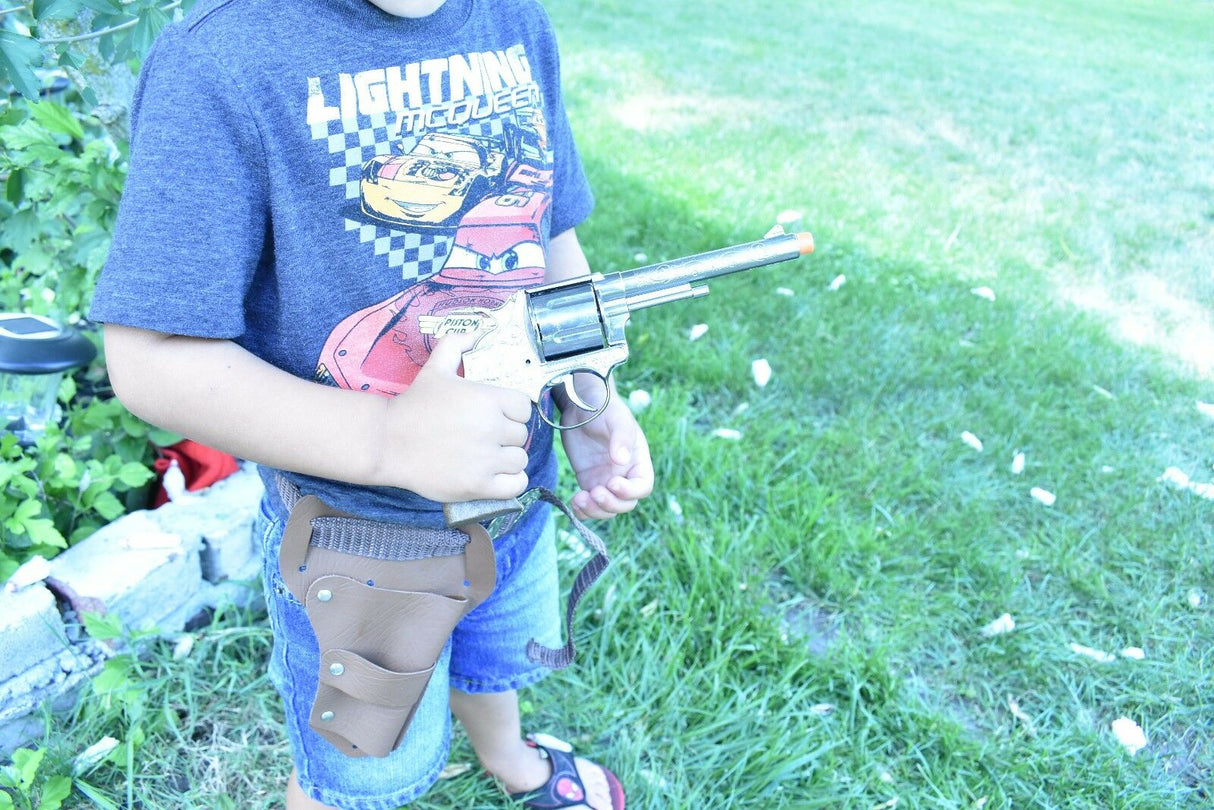 Boy holding a toy pistol and holster set outdoors on green grass for Parris Toys 4711, front view