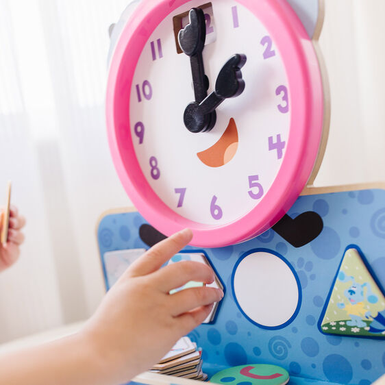 Child's hand interacts with a colorful, magnetic clock toy for Melissa and Doug 33014