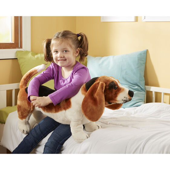 Girl sits on bed with large stuffed Basset Hound dog toy for Melissa and Doug 4866