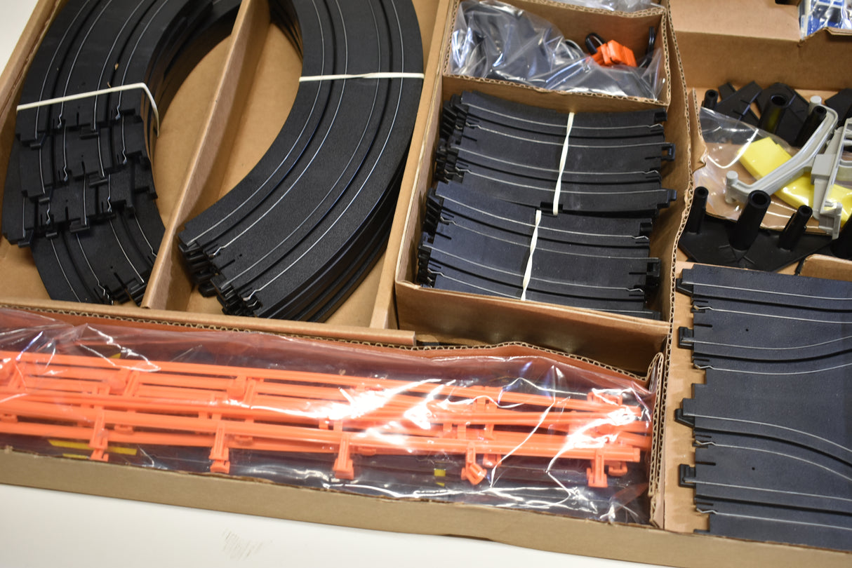 Slot car track pieces and accessories in open cardboard box for Tomy AFX AURORA 9114M