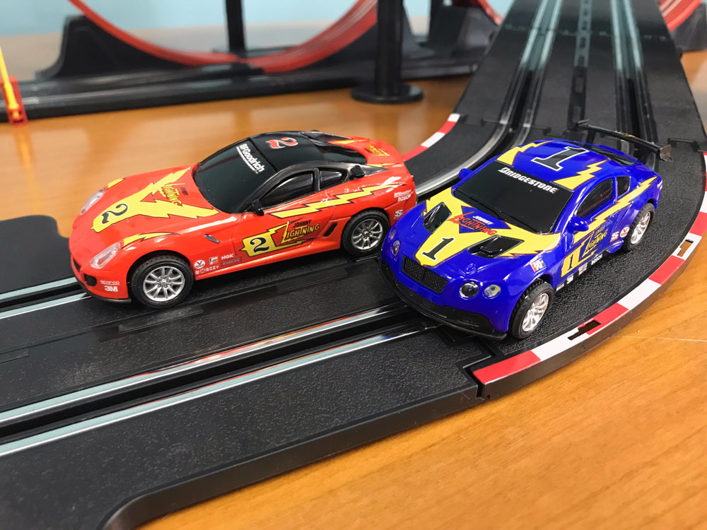 Two red and blue race cars on a black slot car track for EXCLUSIVE JLRS001
