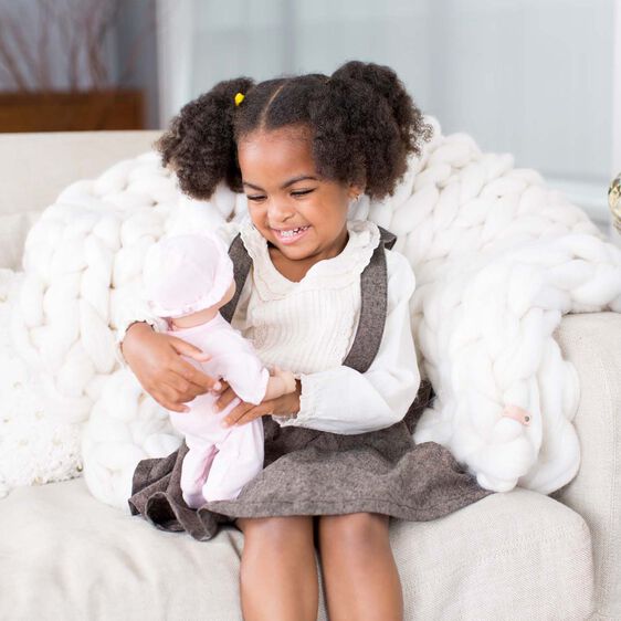 Girl with dark curly hair smiles while holding a baby doll on a white couch for Melissa and Doug 4881