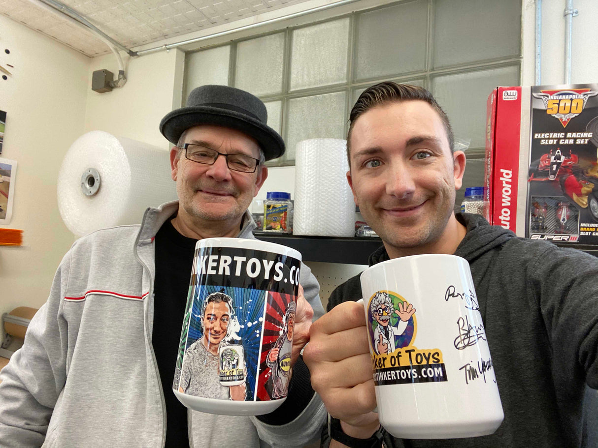 Two men smile with mugs featuring cartoon designs