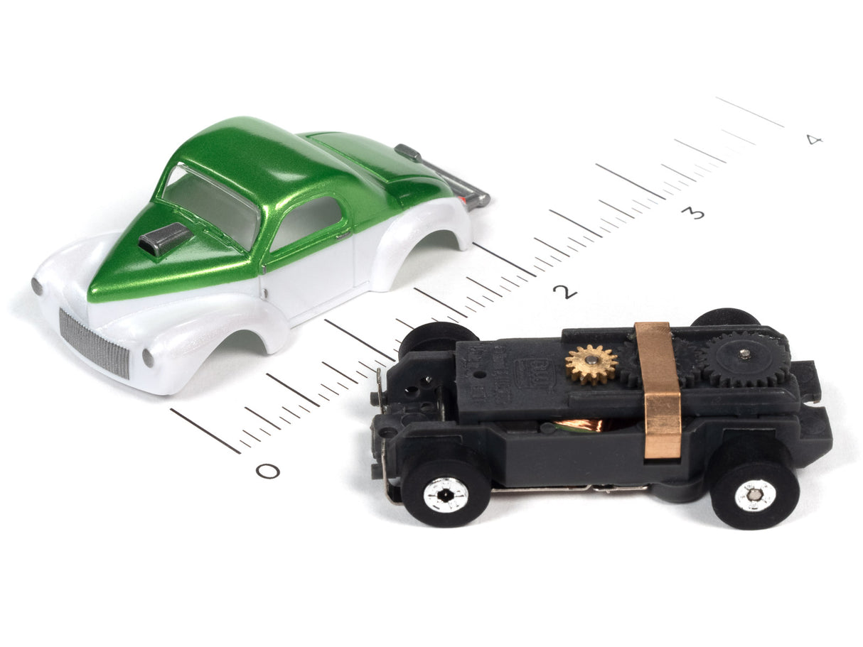 Green and white classic car model next to a black, mechanical car model on a ruler for Auto World SC360