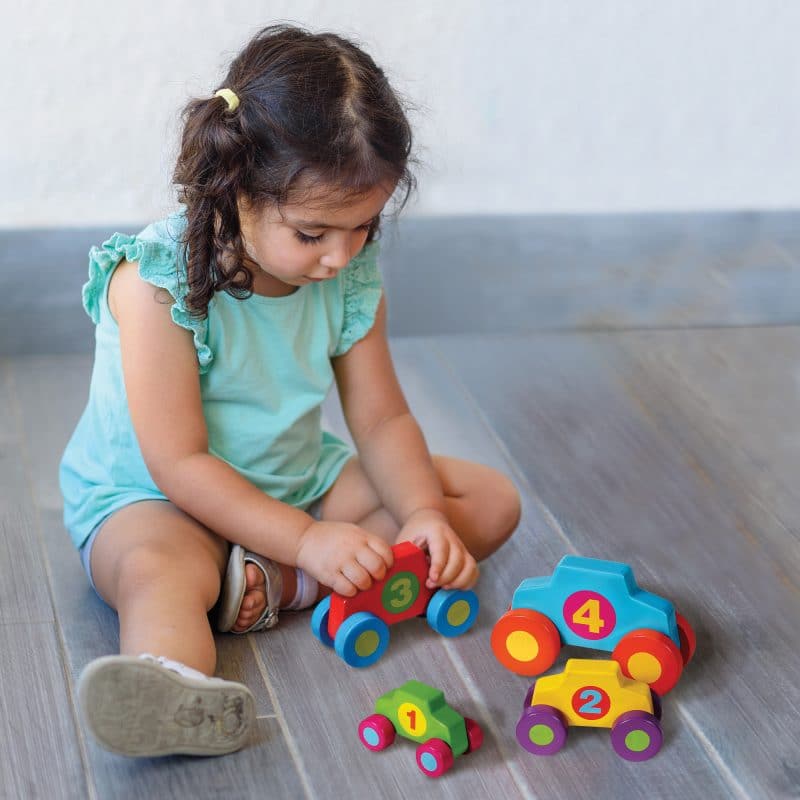 Girl plays with colorful, numbered stacking and play cars on a wooden floor for Schylling SPLC