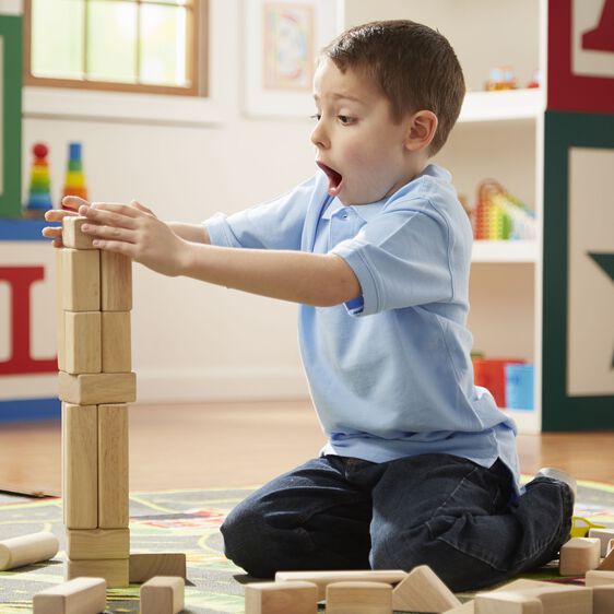 Boy building tall tower with wooden unit blocks, focused expression for Melissa and Doug 503