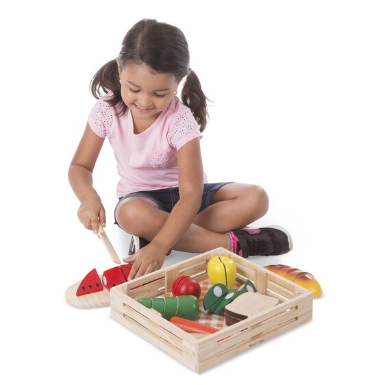 Girl plays with wooden play food, pretending to cut vegetables for Melissa and Doug 487