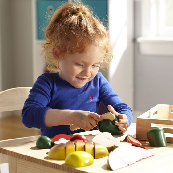 Child plays with wooden food, pretending to cut vegetables on a play kitchen set for Melissa and Doug 487