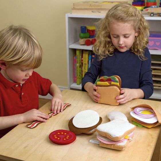 Children play with felt food, assembling pretend sandwiches on a wooden table for Melissa and Doug 3954