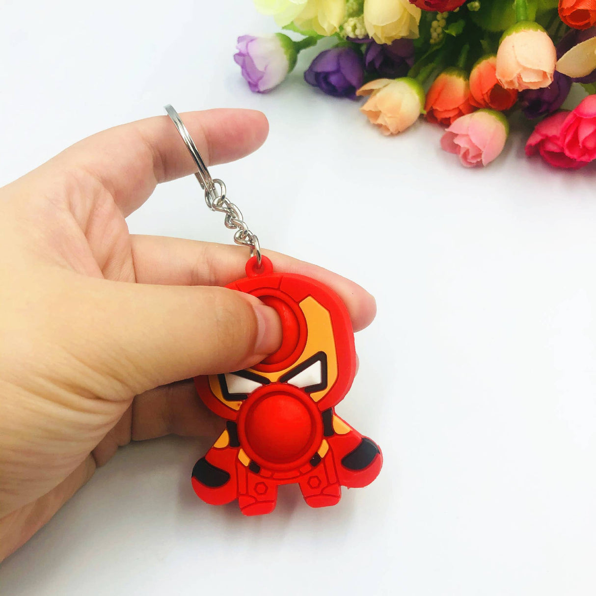Red character fidget keychain held in a hand, with flowers in the background for Faire FH2928