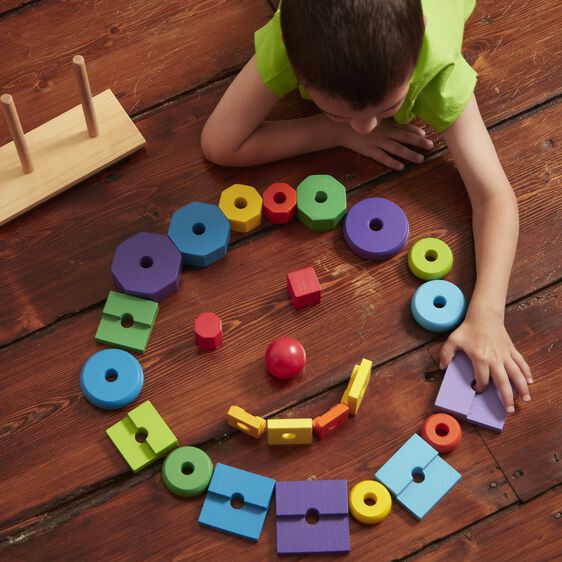 Colorful geometric stacking toy arranged in a circle on a wooden floor for Melissa and Doug 567