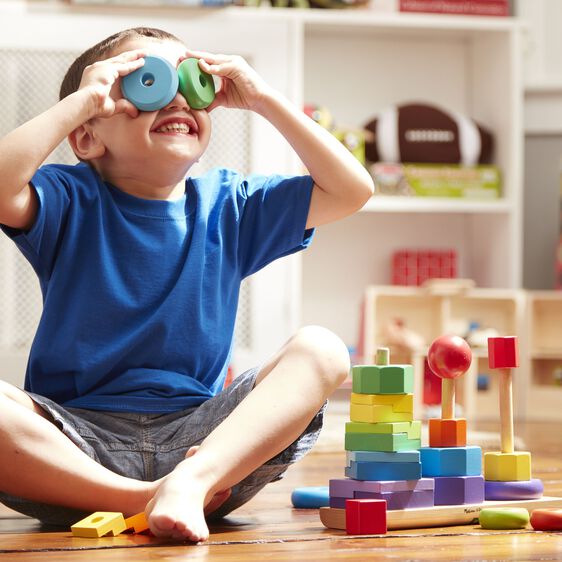 Boy plays with colorful stacking toy blocks on a wooden floor for Melissa and Doug 567