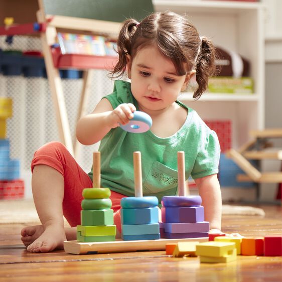 Young girl plays with colorful, stacking geometric toddler toys on a wooden floor for Melissa and Doug 567