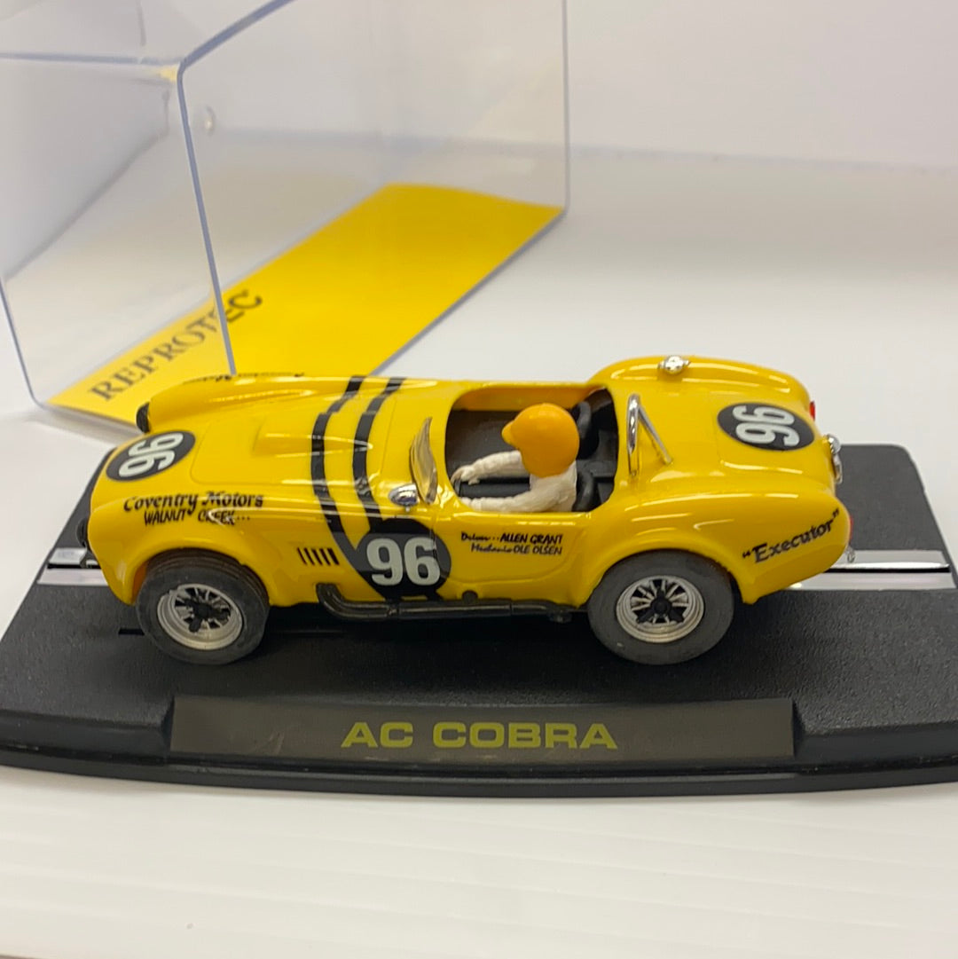 Yellow 1964 AC Cobra slot car on a display base for REPROTEC RT/1964, front view