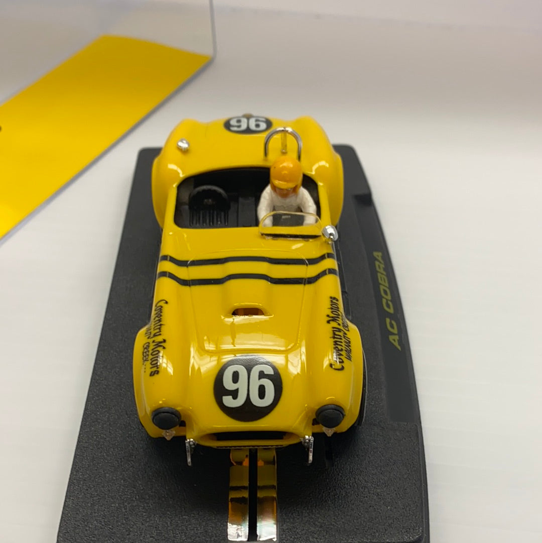 Yellow 1964 AC Cobra slot car on a black display base for REPROTEC RT/1964, front view
