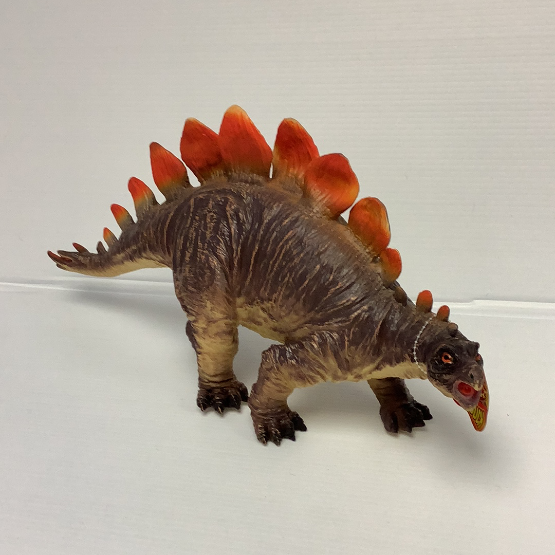 Stegosaurus toy dinosaur with red plates, standing on a white surface for IMEX Model Company IMX49403