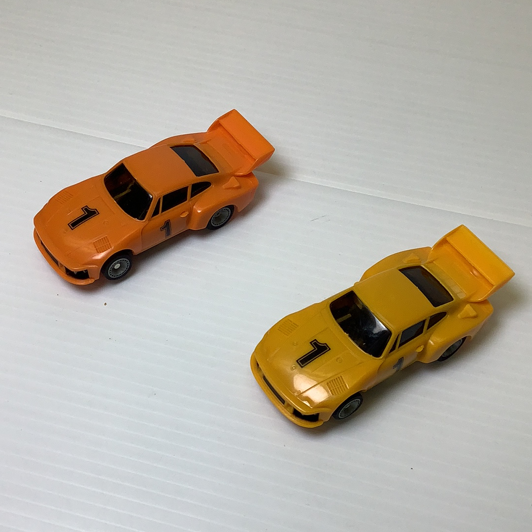 Two slot car scale model cars, one orange and one yellow, displayed on a white surface for Bachmann BAC0002