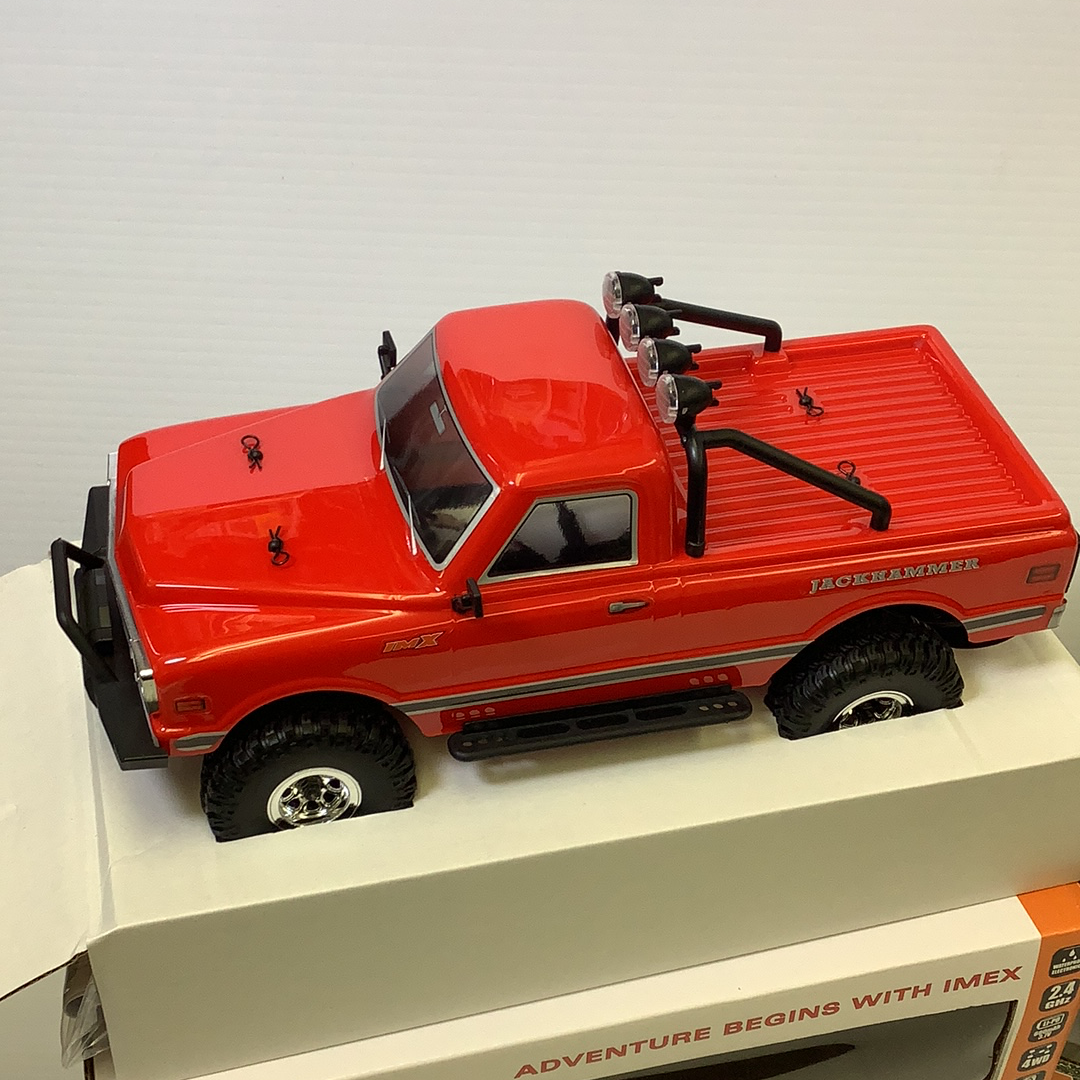 Red toy crawler jackhammer with off-road tires on a white surface for IMX IMX25000