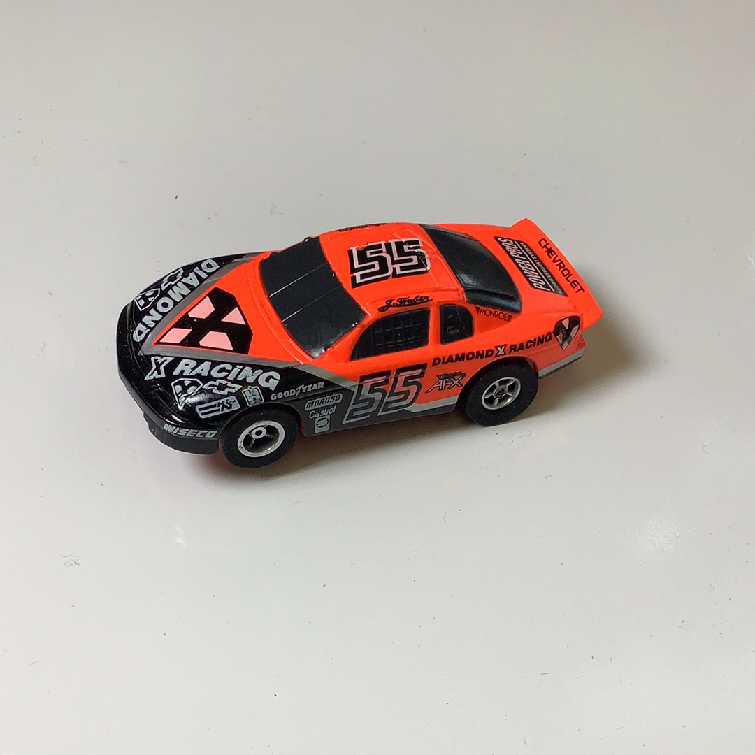 Orange and black slot car race car, number 55, on a white surface for Aurora / AFX / Tomy 9870