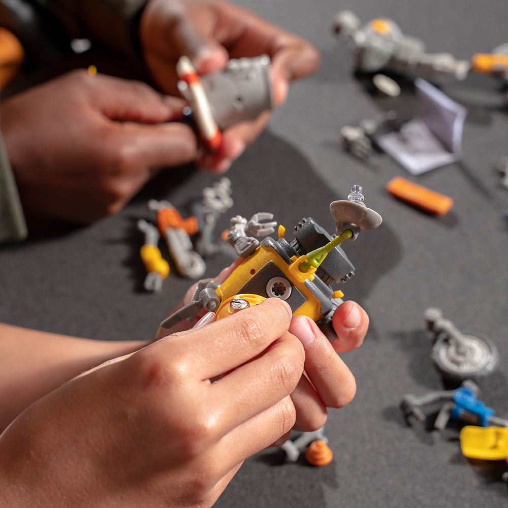 Hands assembling a small, mechanical robot toy with various junk parts for HexBug 430-6843