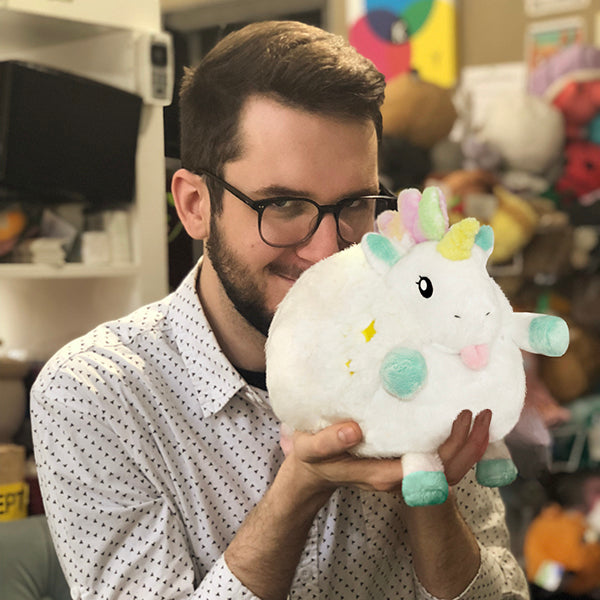 Man smiles, holding a small, white, plush unicorn toy for Squishable 104967