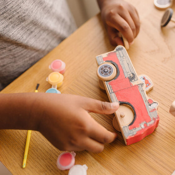 Child crafts a wooden Paw Patrol vehicle on a table with colorful craft supplies nearby for Melissa and Doug 33266