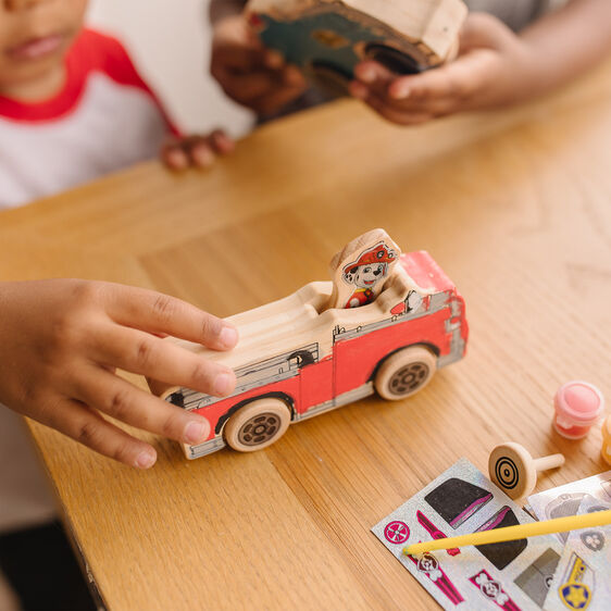 Child's hands near a wooden Paw Patrol vehicle craft kit on a table for Melissa and Doug 33266