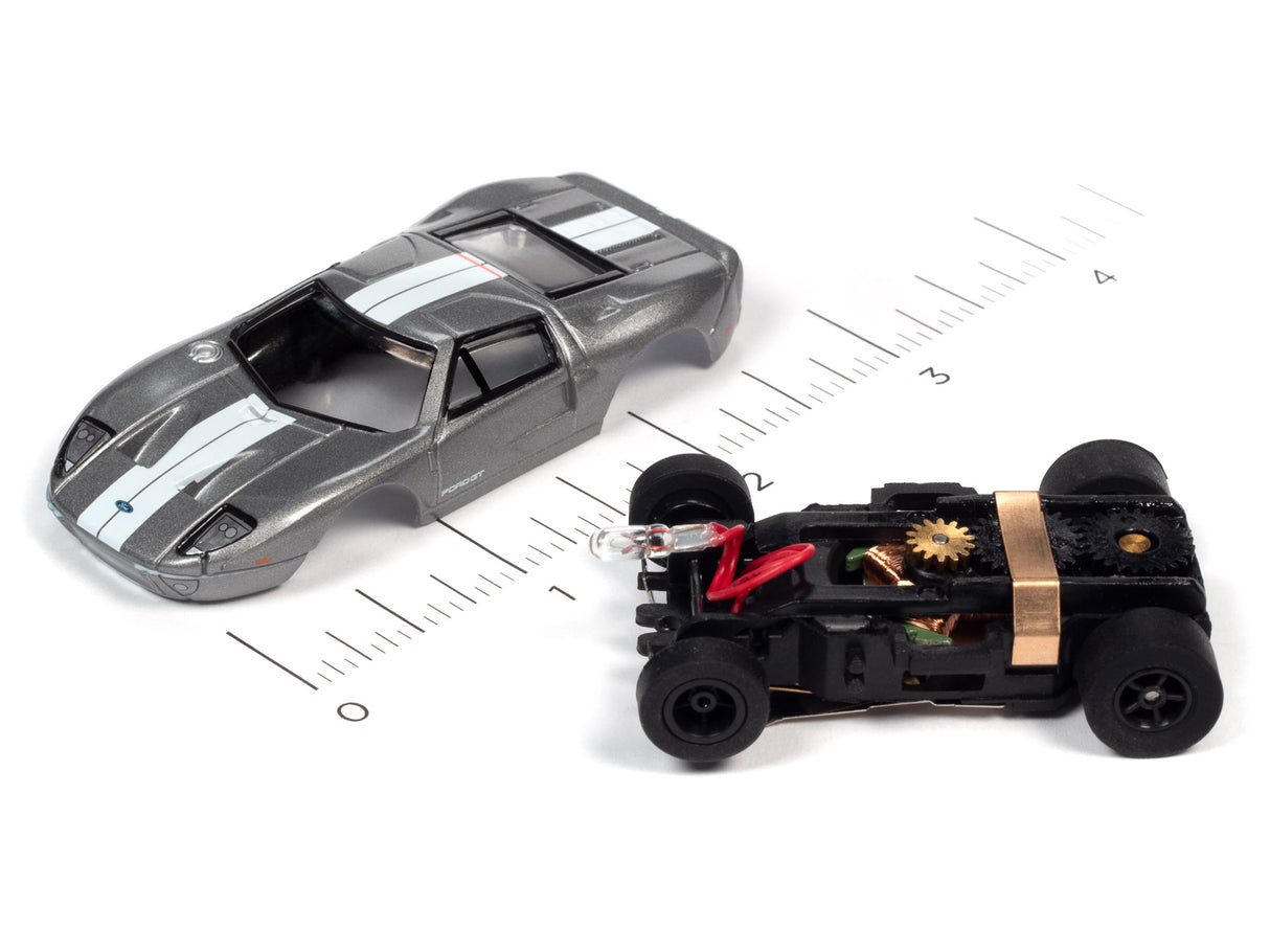 Slot car next to its exposed motor and chassis components on a ruler for Auto World SC366