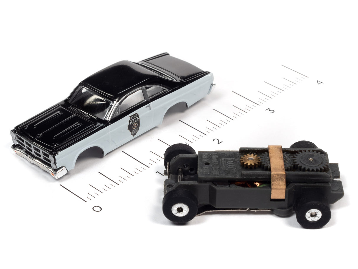 Two toy police cars on a ruler: one black and silver, one black with exposed gears for Auto World SC367