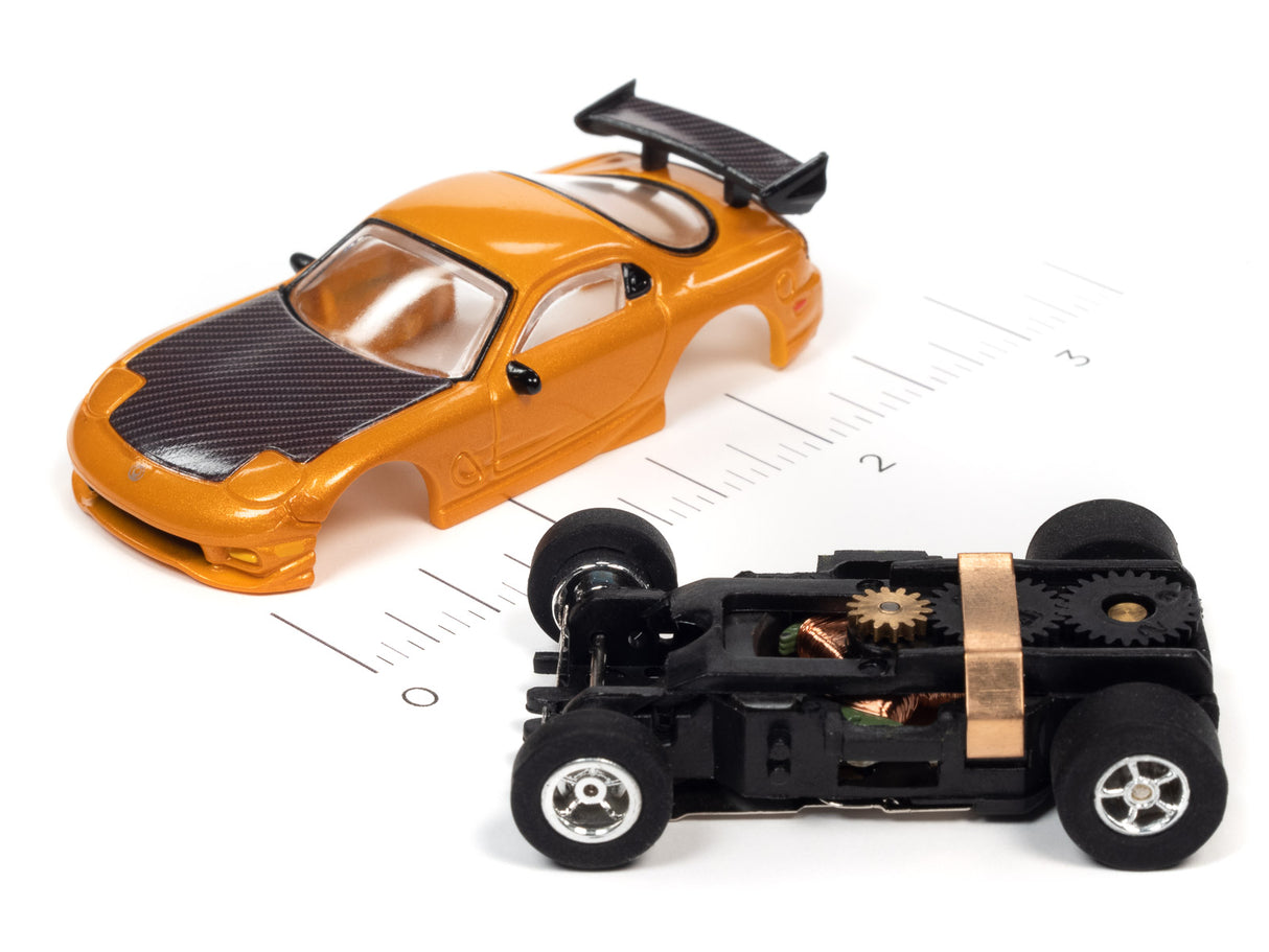Orange slot car and disassembled black car chassis on a ruler for Auto World SC368