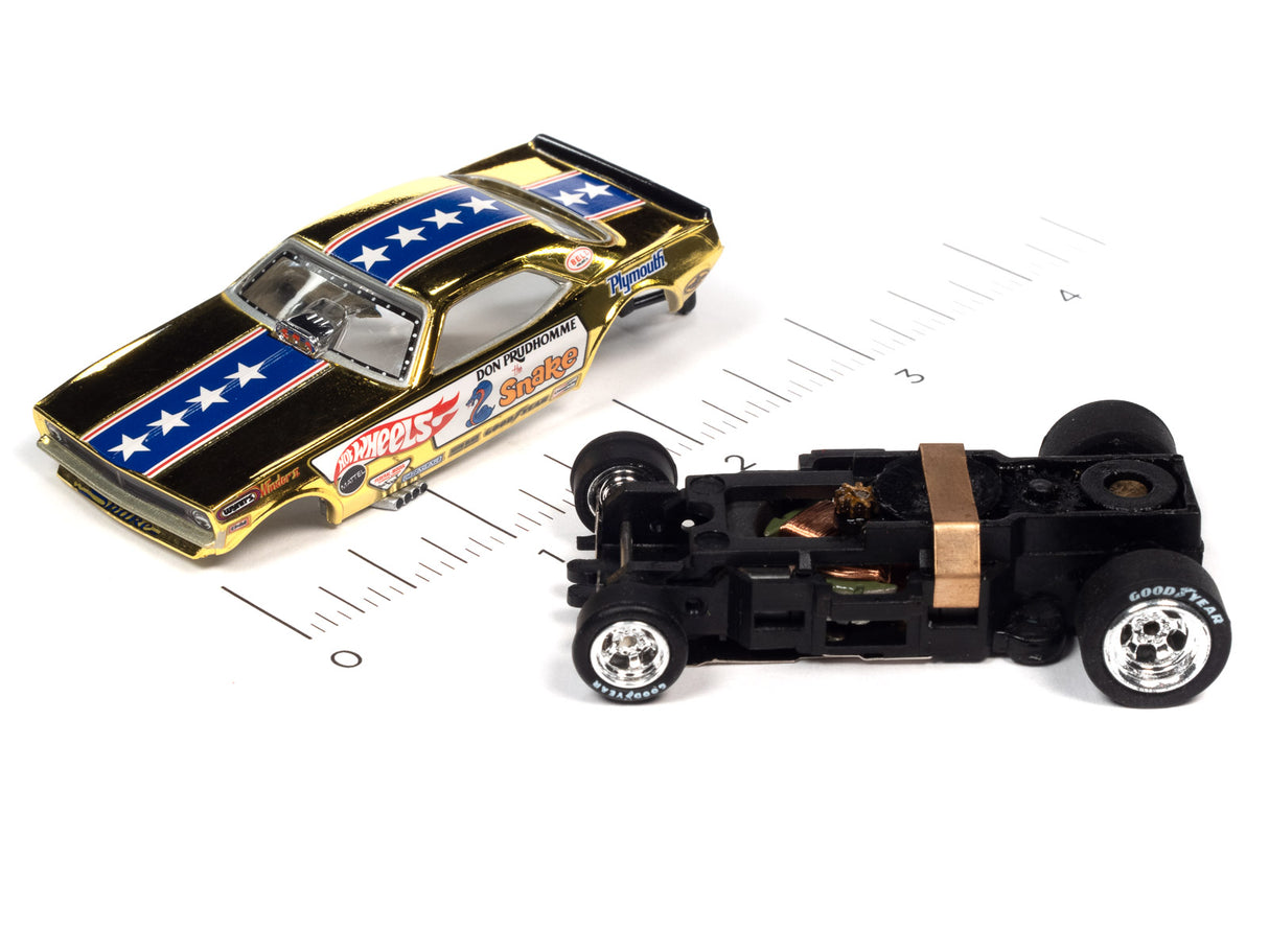 Two slot car race cars, one gold and blue, one black, on a ruler for Auto World SC369