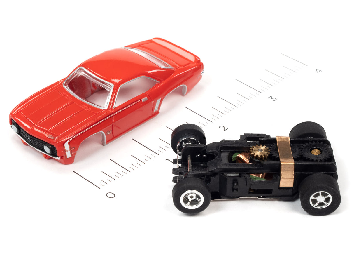Red toy car next to its exposed motor and wheels on a ruler for Auto World SC373