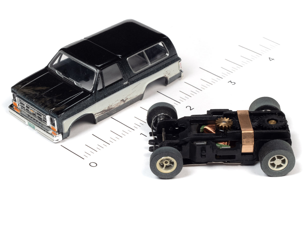 Black and silver slot car next to a black off-road vehicle on a ruler for Auto World SC375