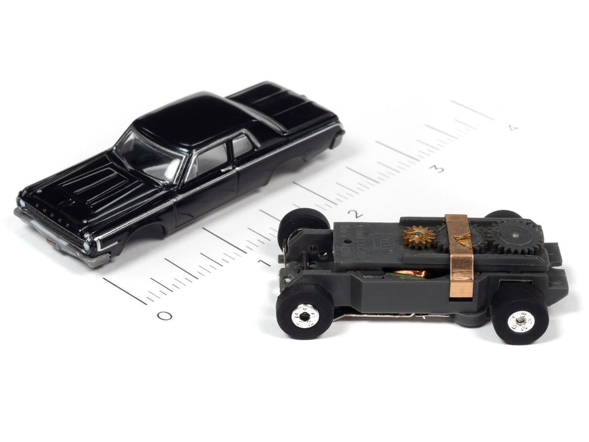 Two black toy cars on a ruler: a sleek sedan and a boxy, mechanical vehicle for Auto World SC379